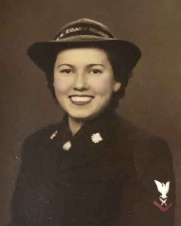 Sepia toned photo of a young woman smiling at the camera wearing a dark uniform. Red trim is visible