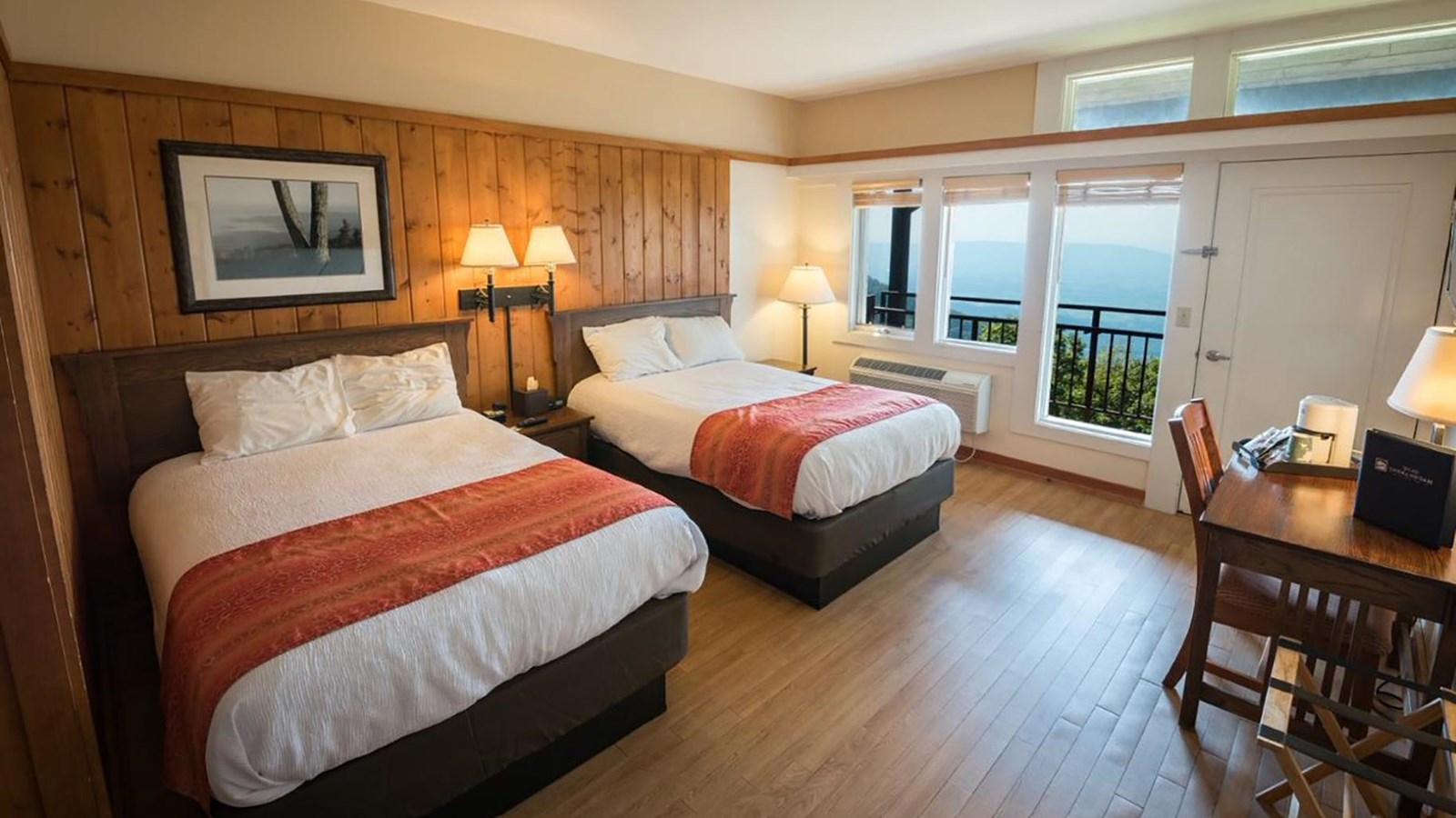 A hotel room with two beds and a view through the window of blue mountains.