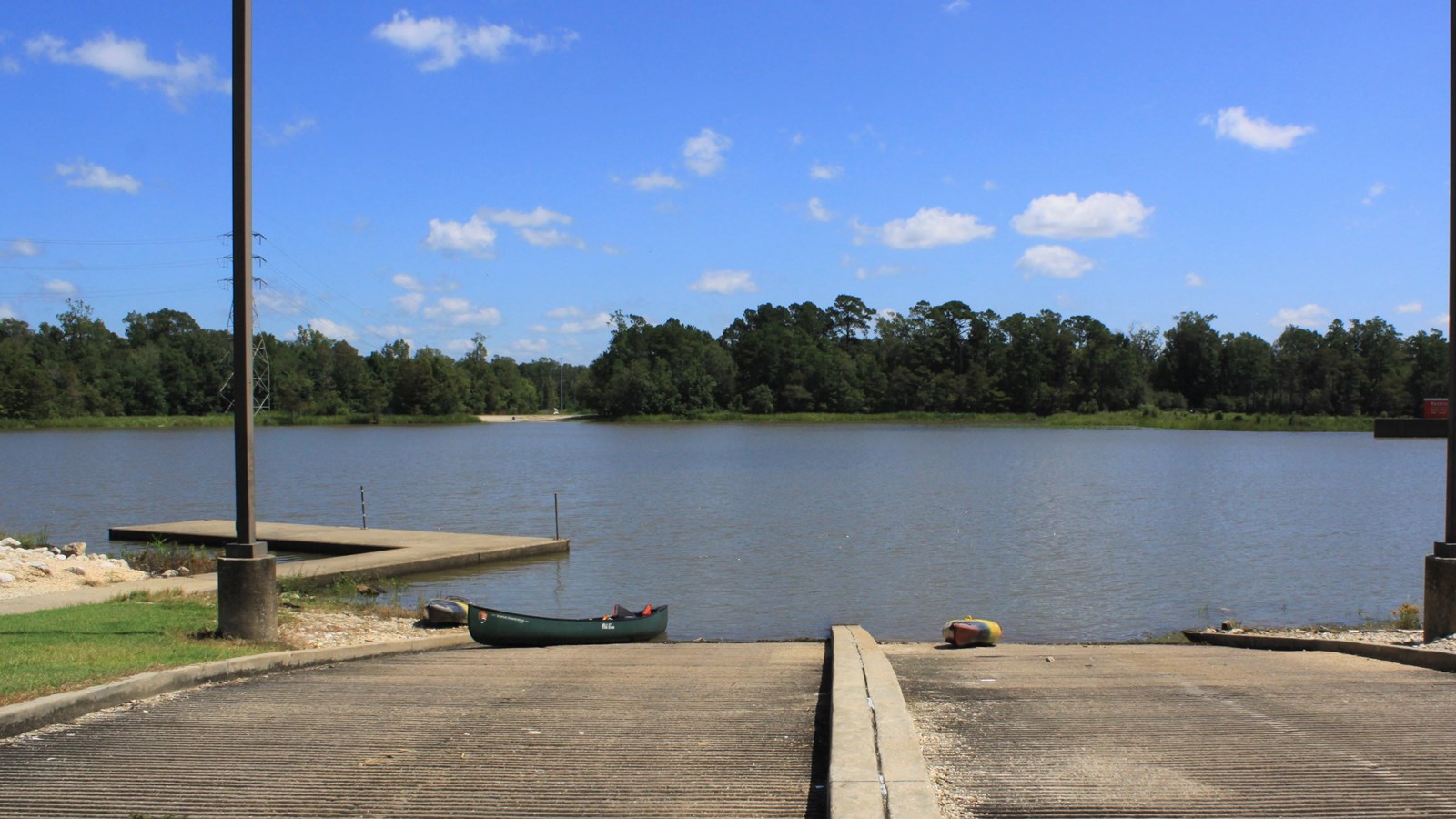 a canoe and a kayak sit at the bottom of a paved boat ramp on a river