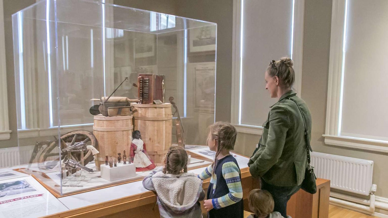 A woman and two small children looking at an exhibit with Old West toys, guns and other objects.