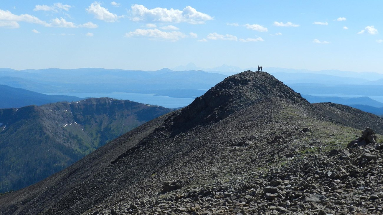 Two hikers enjoying the view of mountains in the distance from the summit of rocky mountain.