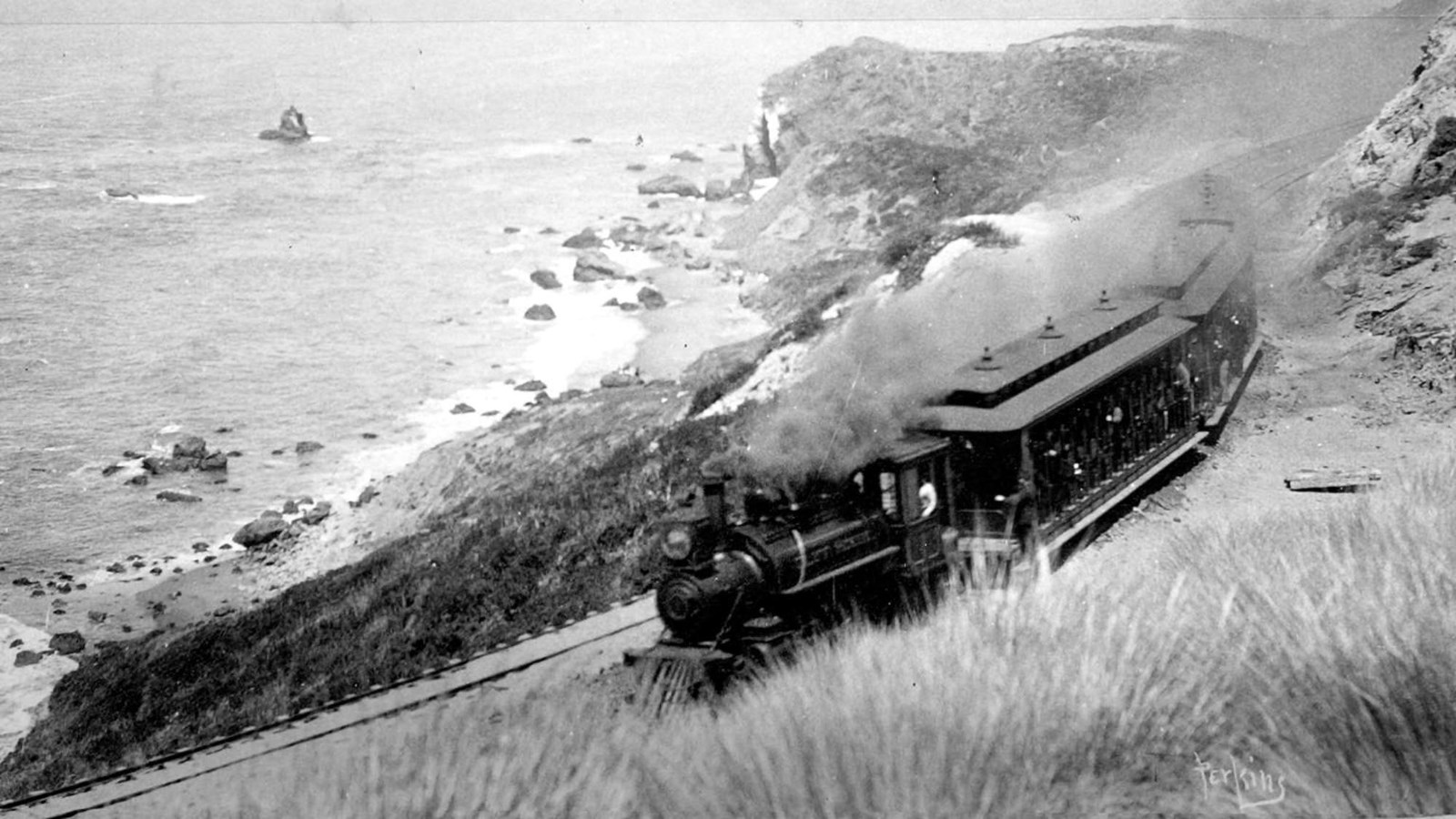 A coal fired steam train on the bluff above the ocean, with the Marin Headlands in the distance.