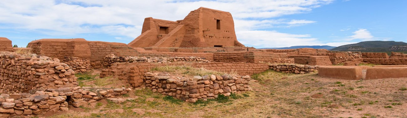 Adobe ruins with stone walls, under a blue sky in a desert setting.