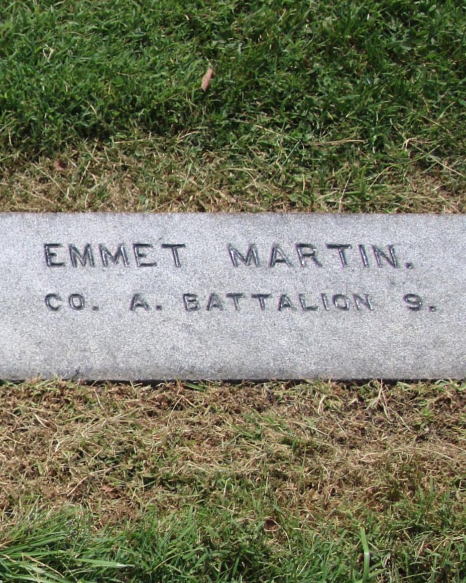 The dark colored gravestone engraved with the name Emmert Martin lays flat with the ground. 
