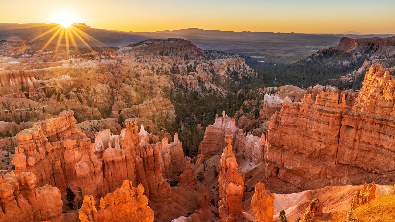 Looking down from above over a scenery of irregular red rocks with the sun rising behind them
