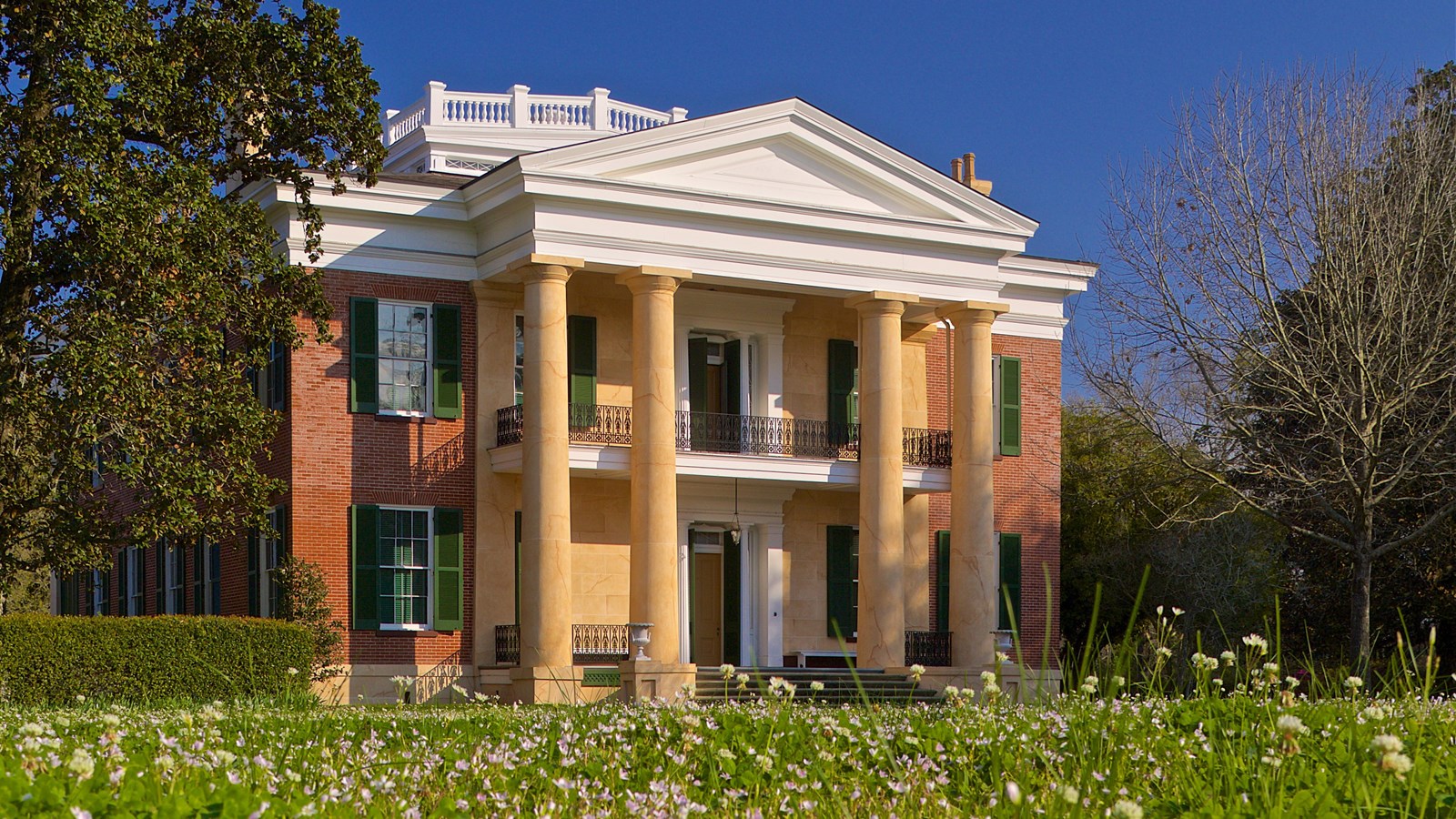 Two-story mansion with first and second story porches, 4 columns, and a widows walk on the roof.