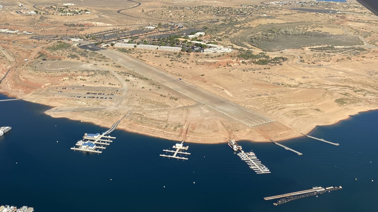Aerial view of many boats moored on a desert lake. A concrete launch ramp does not reach the water