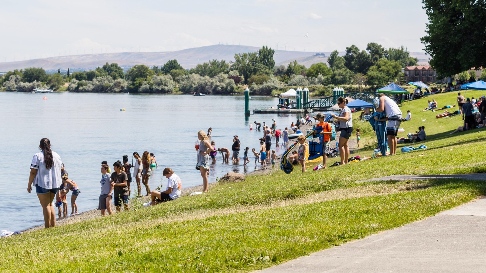 Color photograph of several dozen people, primarily children gathered on a river\'s shore. 