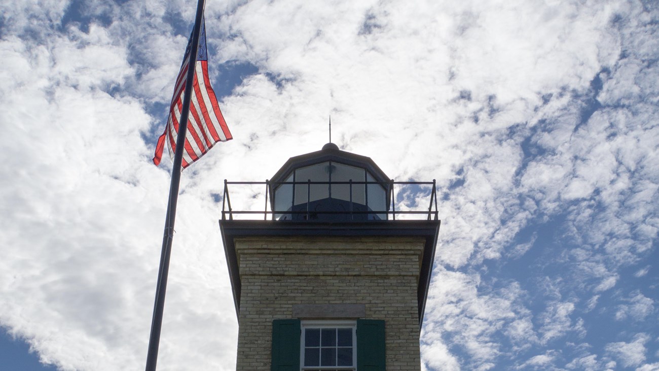 A lighthouse front is in shadows in front of a bright, cloudy sky