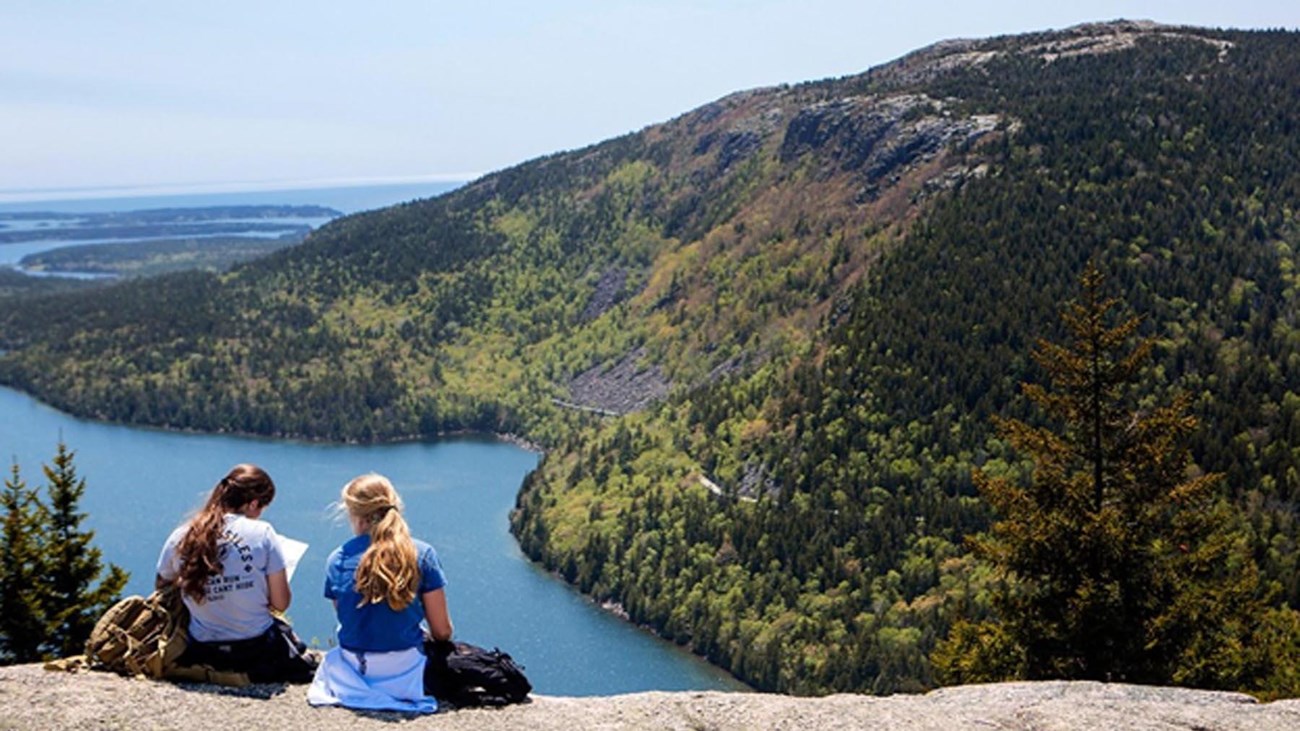 Two hikers sit on the bald granite summit of North Bubble studying a map. 