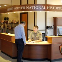 A uniformed ranger at an information desk assists a park visitor.