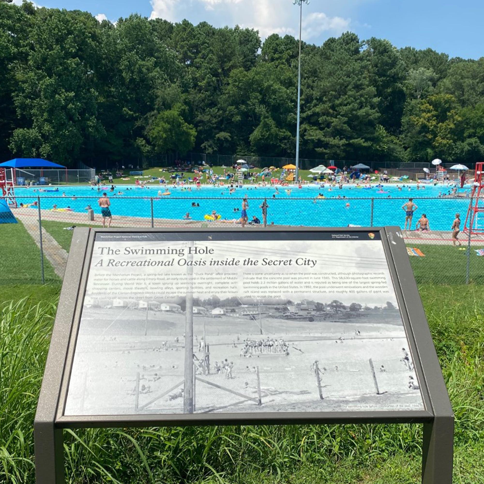 A wayside exhibit in the foreground of a large public pool.