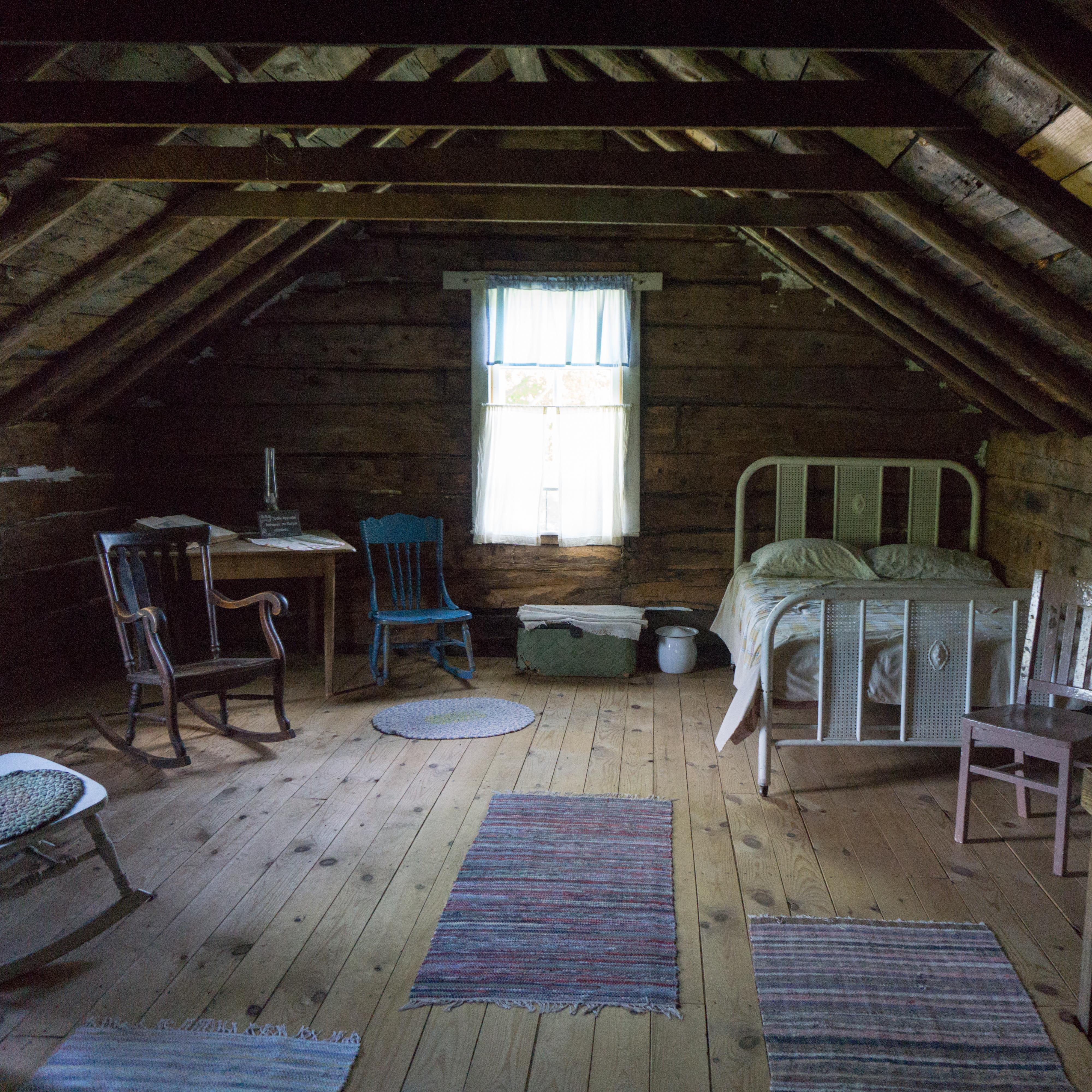 Antique chairs and beds in an attic with a single window and exposed rafters