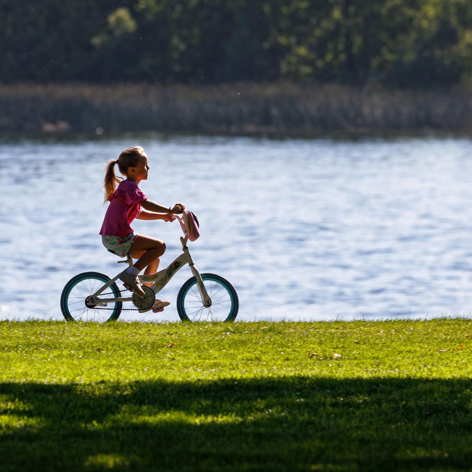 A young girl rides her bike in a grassy area along the river.