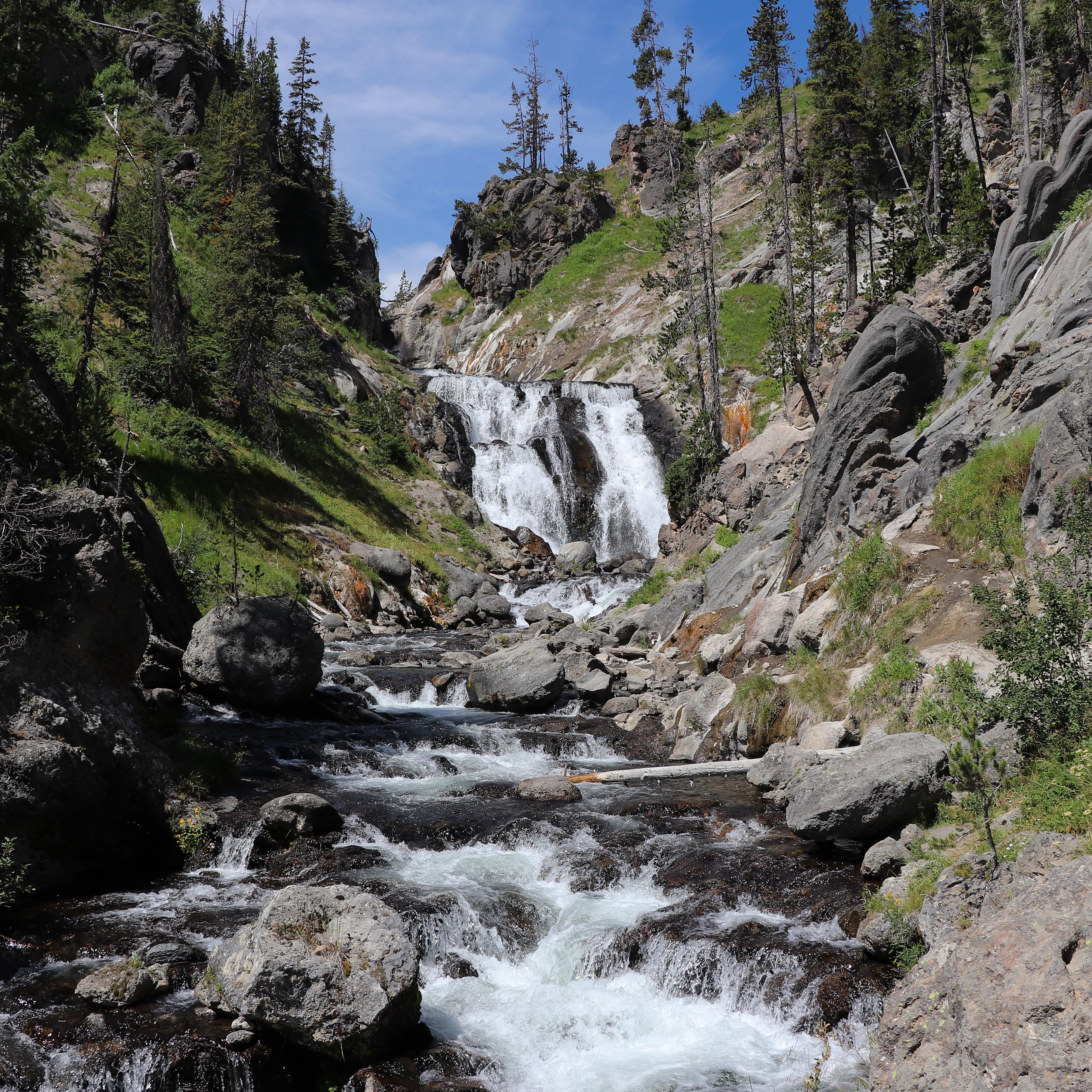 A waterfall cascades over a cliff and flows into a stream down a rocky creek.