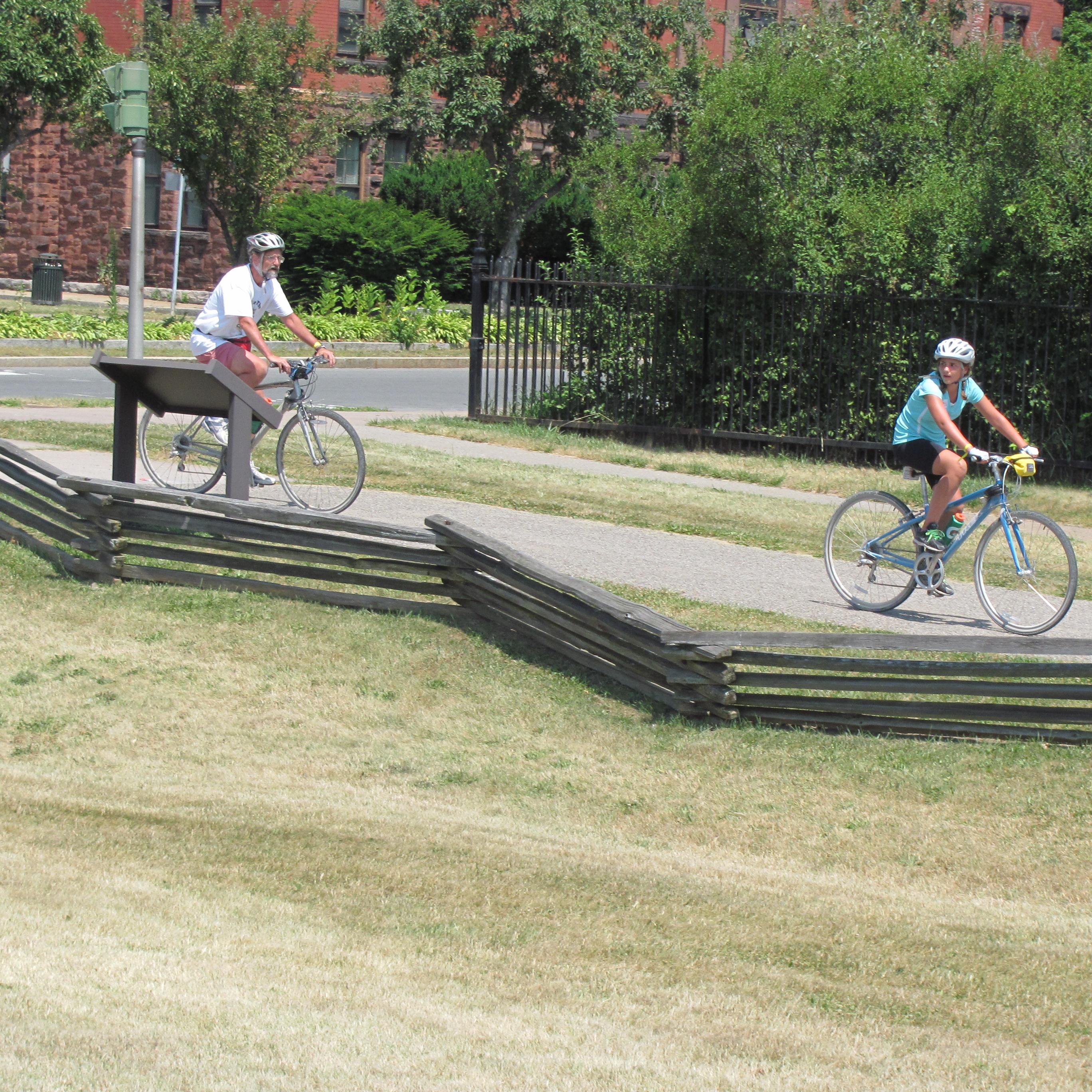 Two people cycle in a line down the park trail.