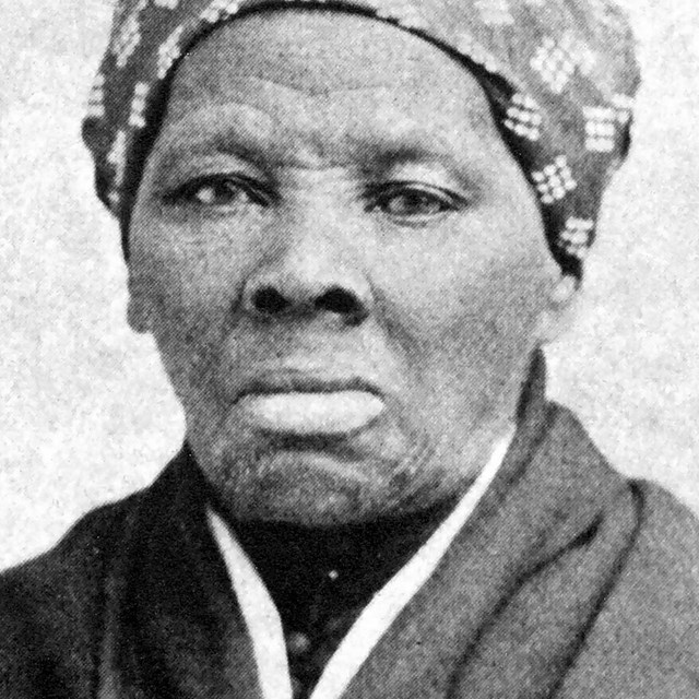 A black and white image of Harriet Tubman. She is looking at the camera. A kerchief on her head.
