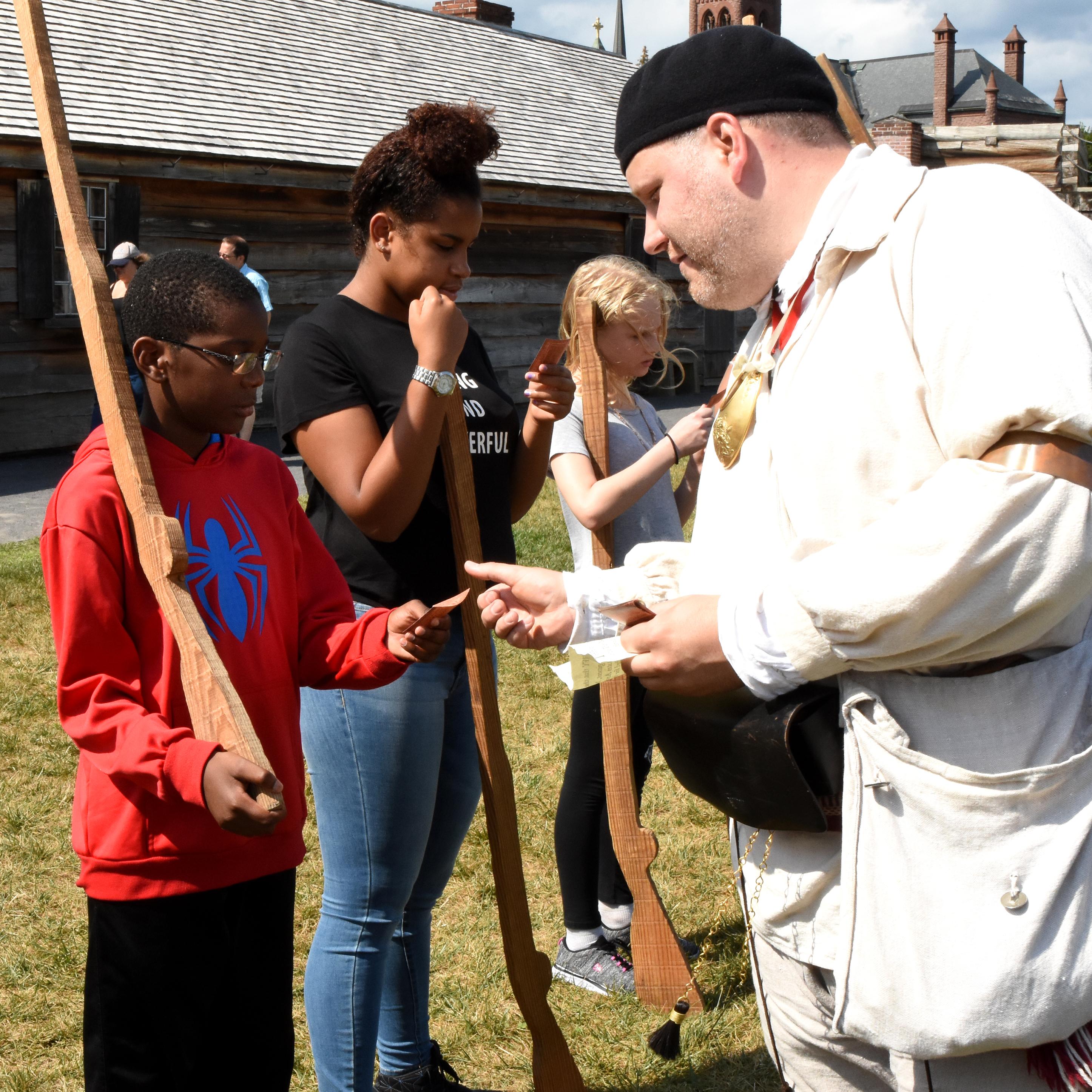 A boy stands opposite from a Continental Soldier, holding a wooden musket