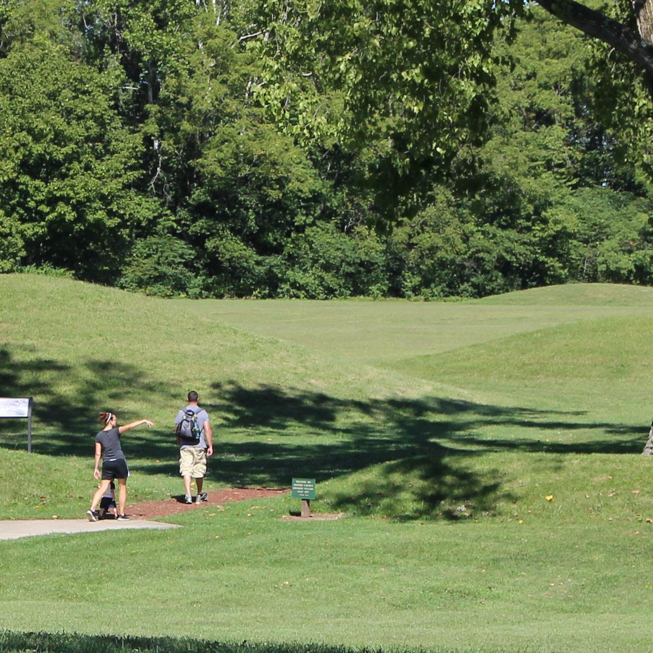 Two people walking into a grass-covered mound area