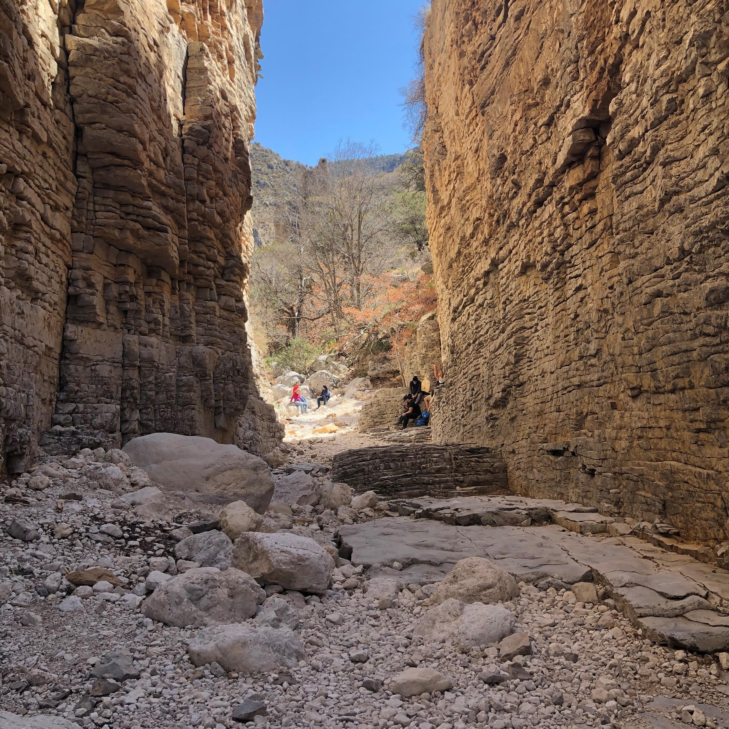 Groups of people in the sunlight at the end of a narrow tall canyon.