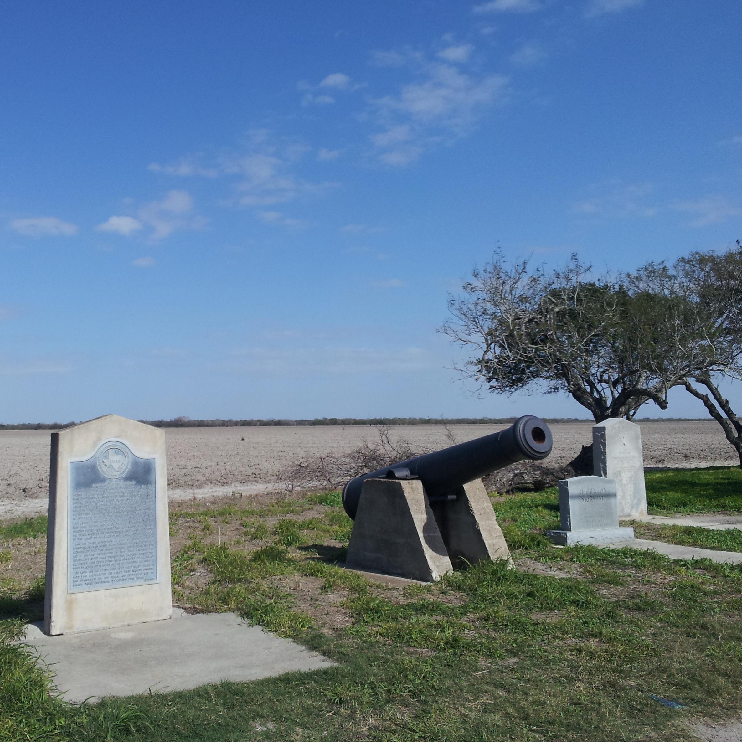 Concrete historical maker next to black siege cannon on concrete base.