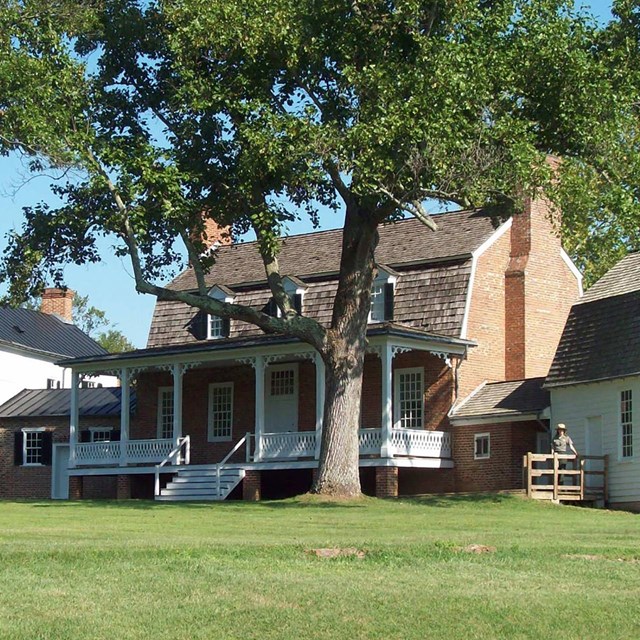 A large brick house with white trim. It has 3 wings with the largest in the center. 