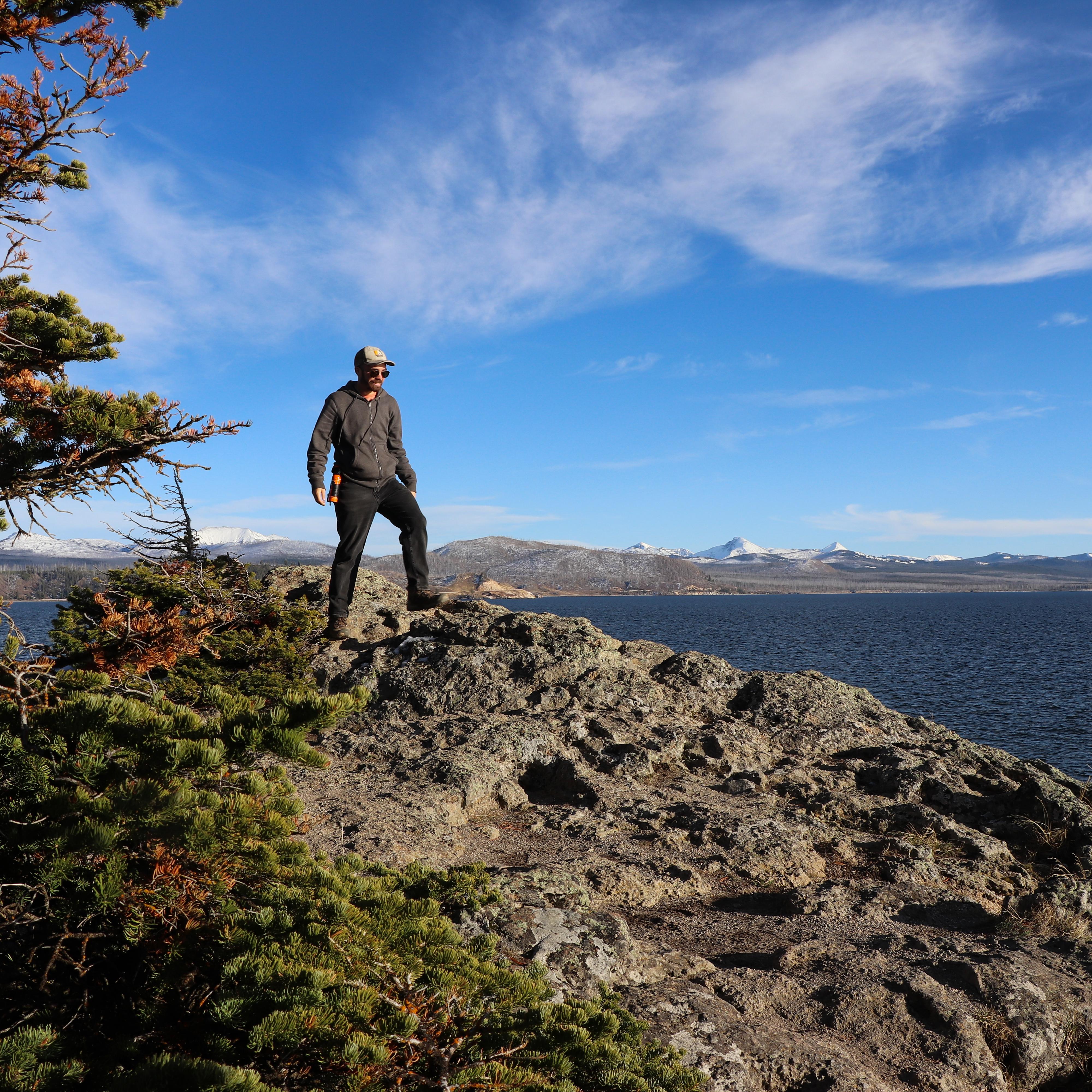 A hiker walks across a rocky outcropping above a large lake.
