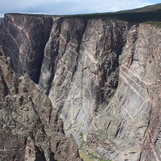 Canyon walls with grey, brown, and pink intrusions stand tall above a river.