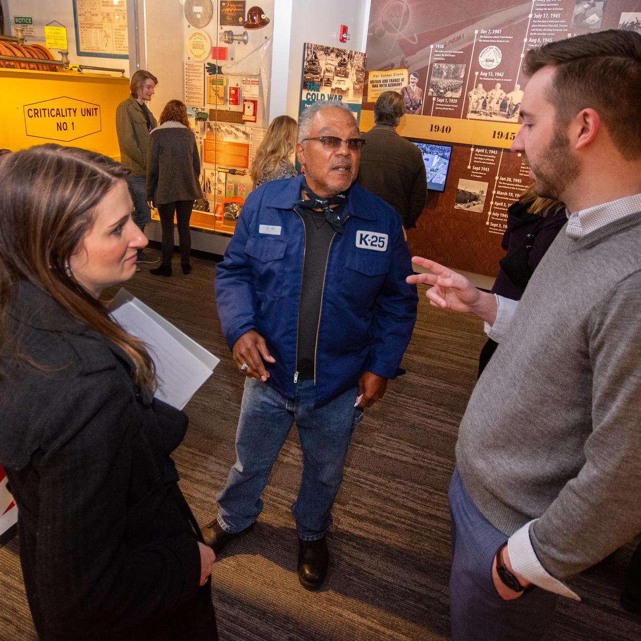 Two men and one woman talking to each other inside a museum.