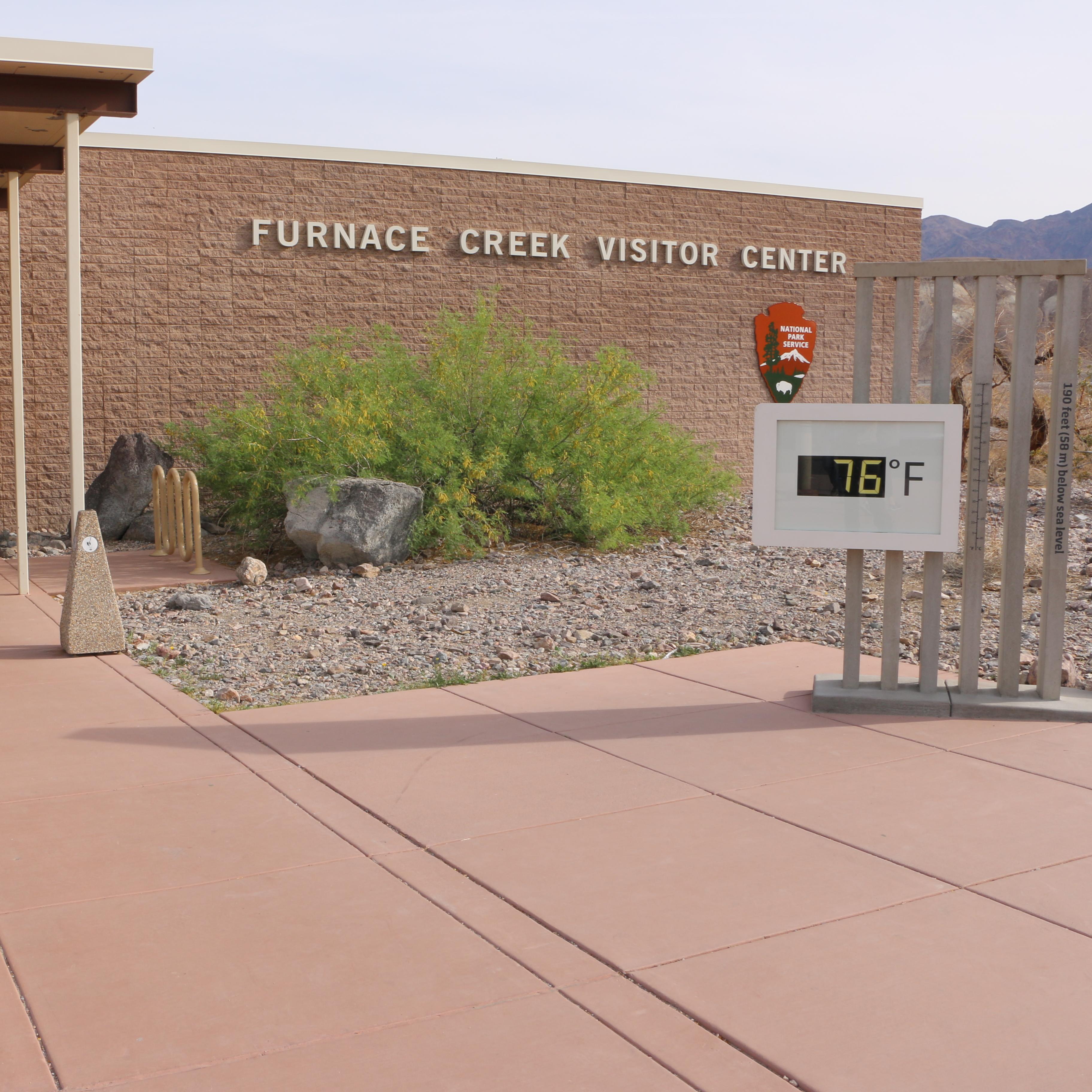 A brick building with a covered path, and a large thermometer out front. 