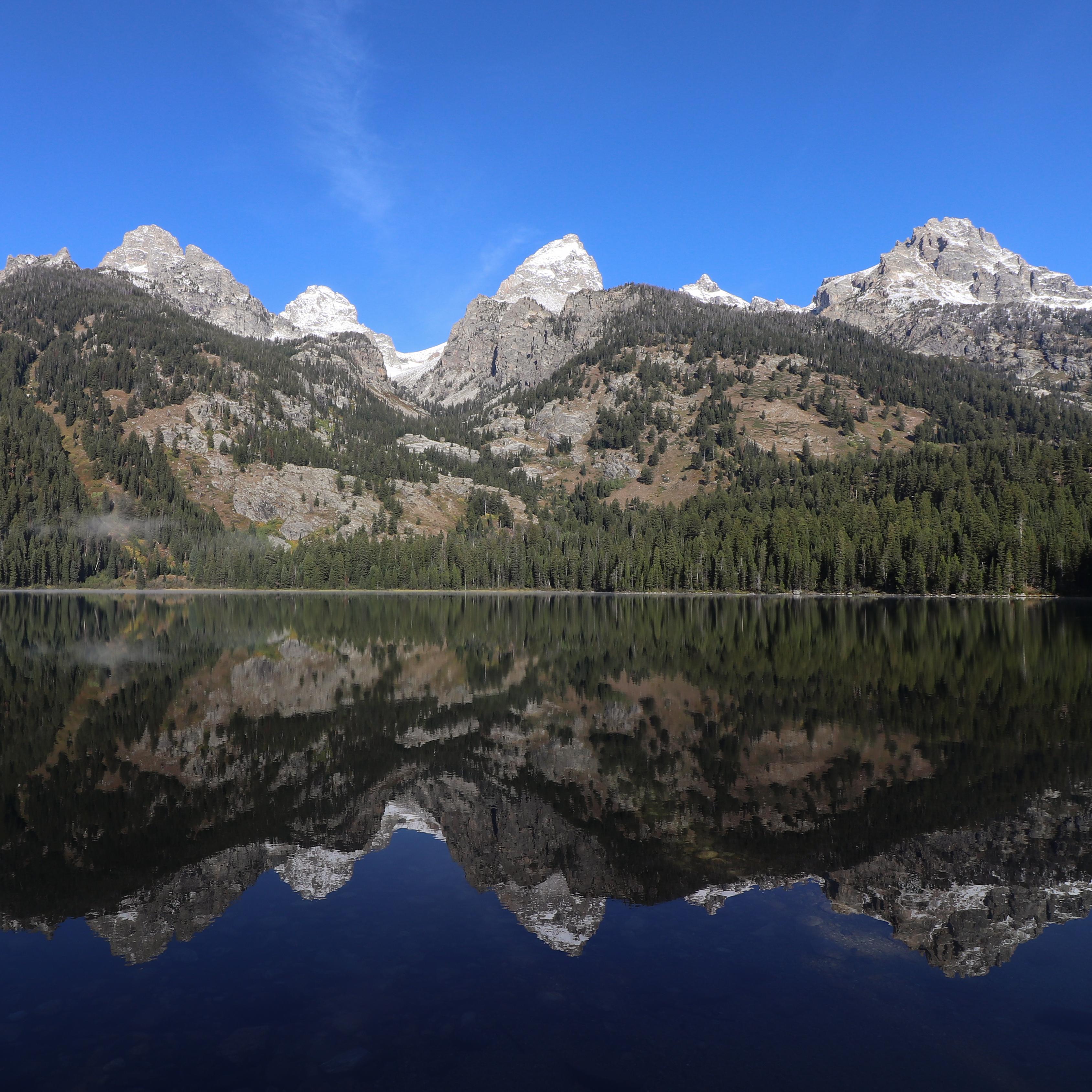 A lake sits at the base of a mountain range with a near perfect reflection on its calm surface.
