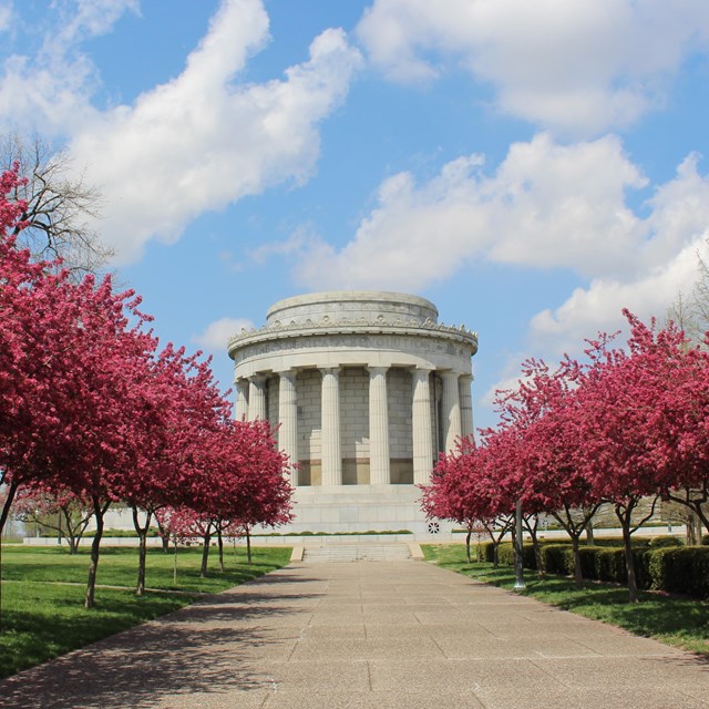 Sidewalk lined by crabapple trees flowering pink leading to the Clark Memorial