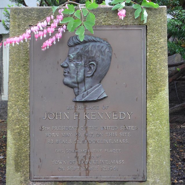 A large stone marker with a bronze silhouette of JFK, similar to that seen on the US dime. 
