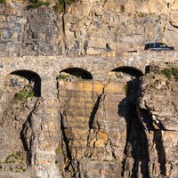 Car drives uphill over triple arched stone bridge