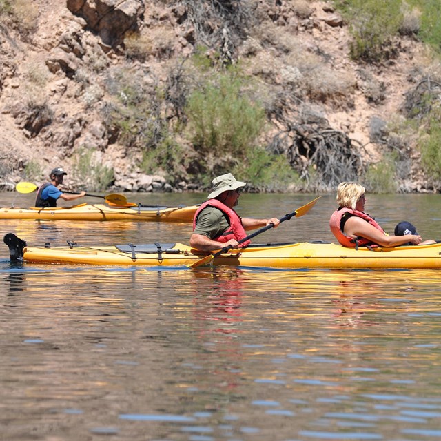 Three people padding kayaks on desert river