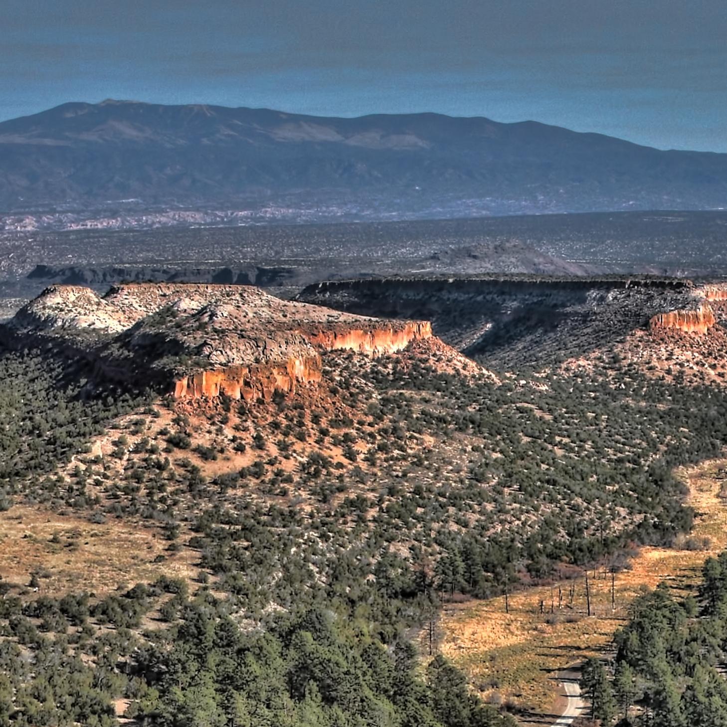 A panoramic view shows mesas dotted with vegetation and mountains in the background.