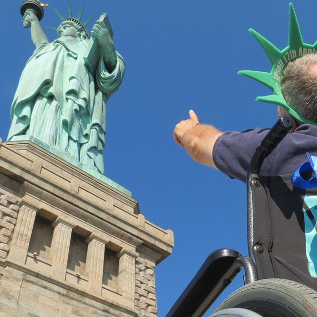 Visitor sitting and pointing at the Statue of Liberty. 