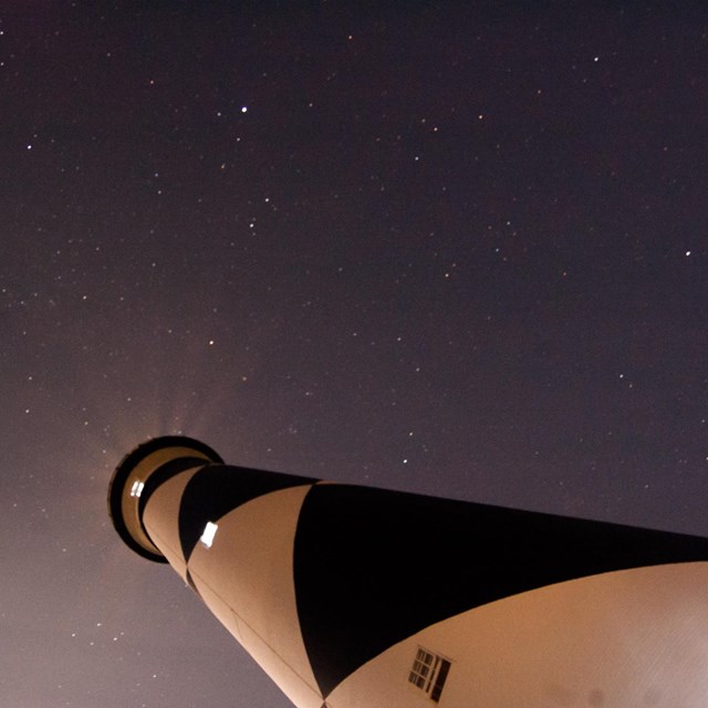 Black and white lighthouse from below against starry sky