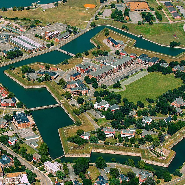 An aerial shot of a peninsula. A star-shaped brick building surrounded by modern structure at center