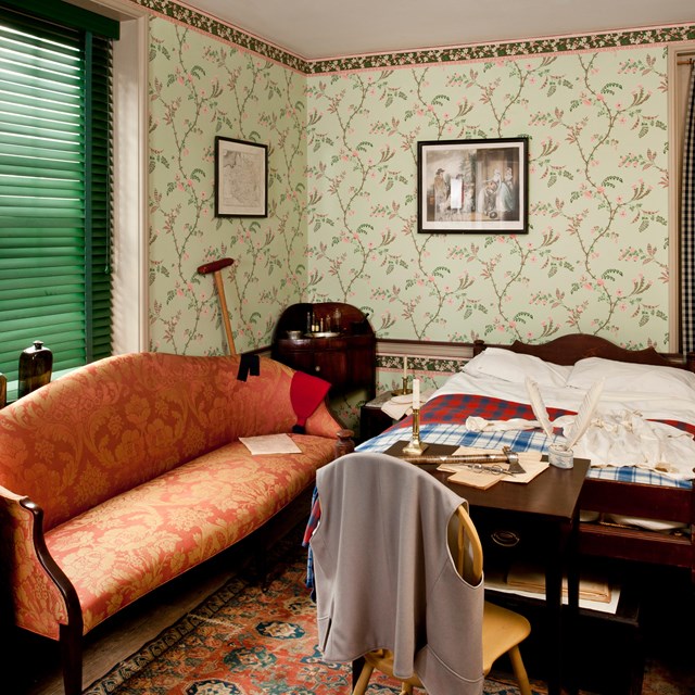 Color photo of a recreated 18th century bedroom showing bed, sofa, desk, and chair.