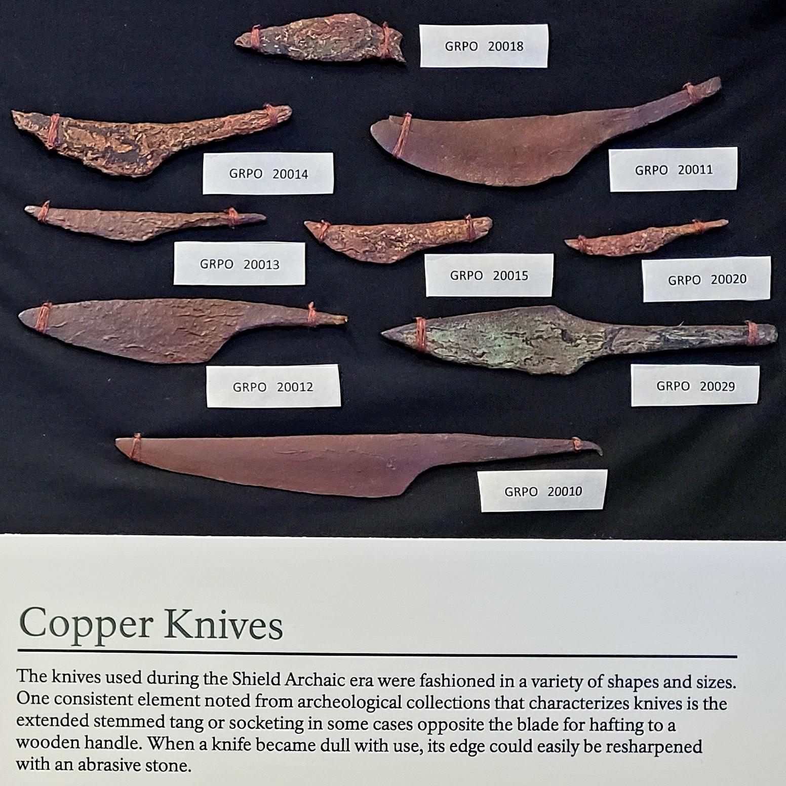Weathered copper projectile point and knives in a display case.