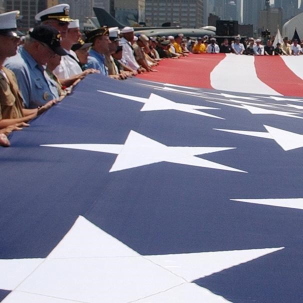 Large American flag held horizontal to the ground by sailors and veterans.