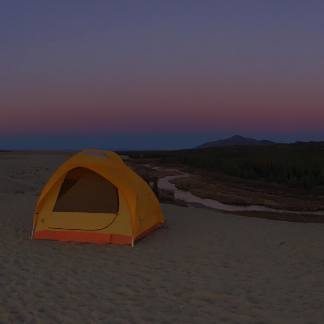 Several tents set up on the Great Kobuk Sand Dunes at dusk.