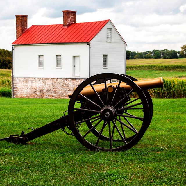 Cannon in field in front of farmhouse. 