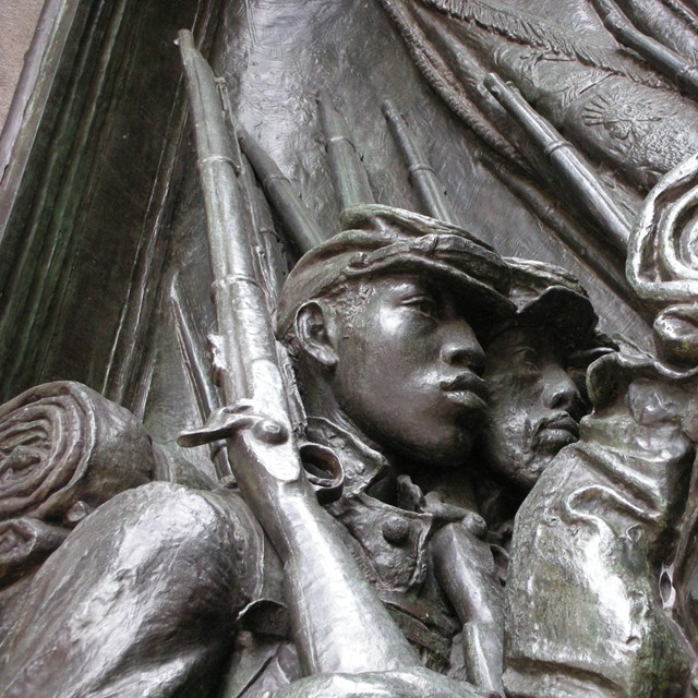 A profile relief of two young soldiers with chiseled features and their equipment. 