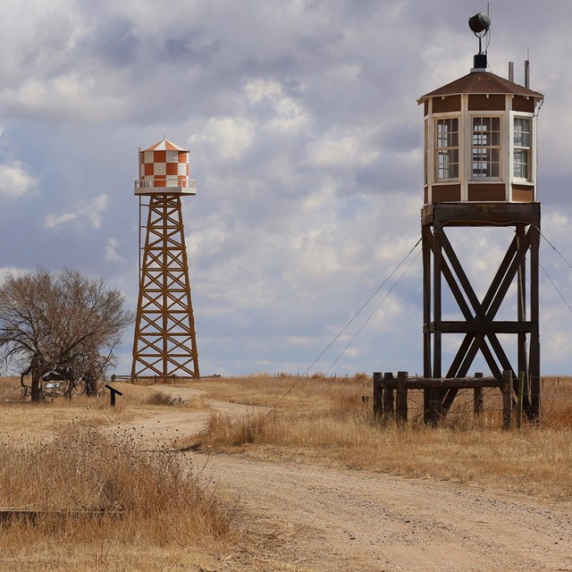 A road leads between a barrack on the left and a guard tower on the right towards a watertower