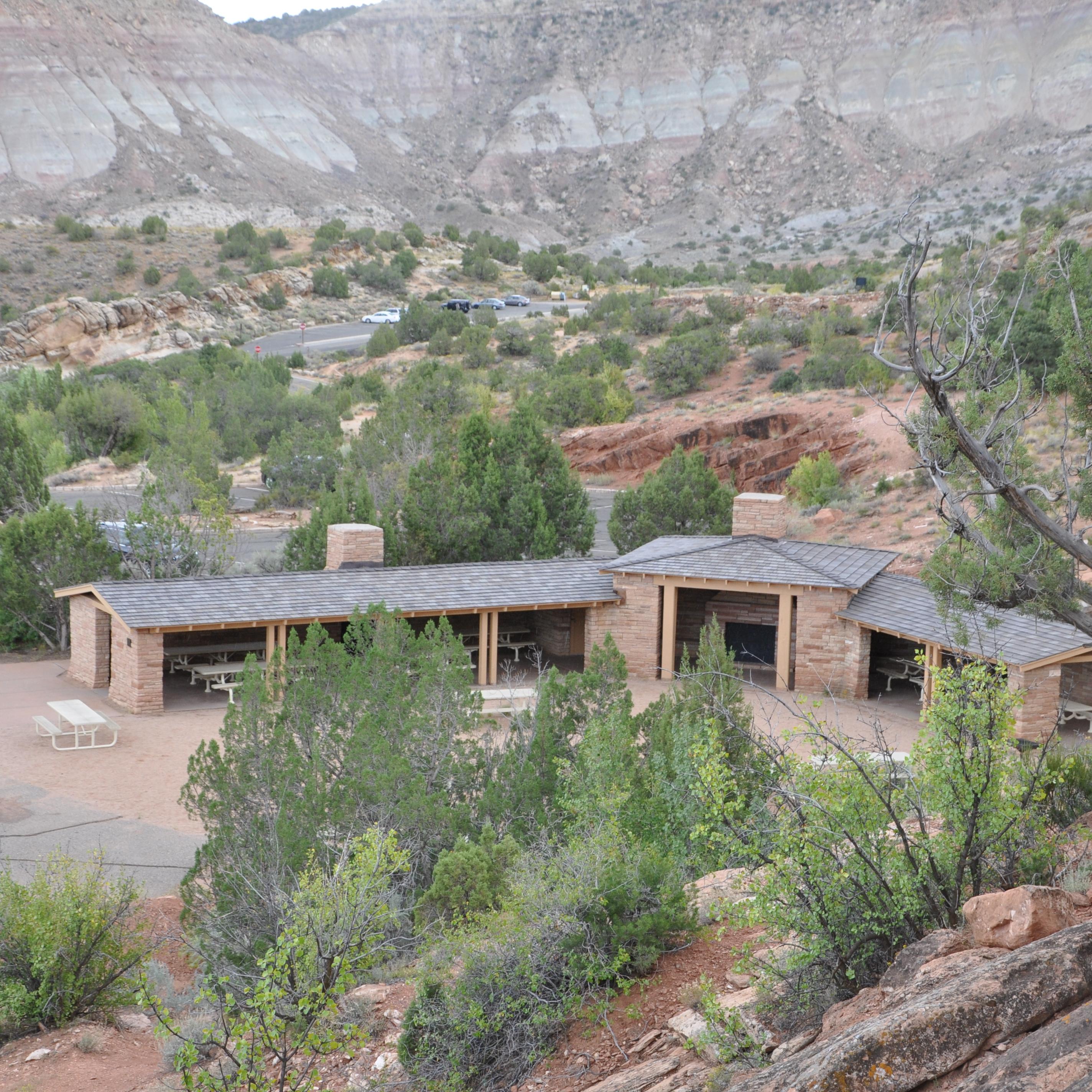 Stone structure with open walls covering picnic tables, in an open area surrounded by canyon walls