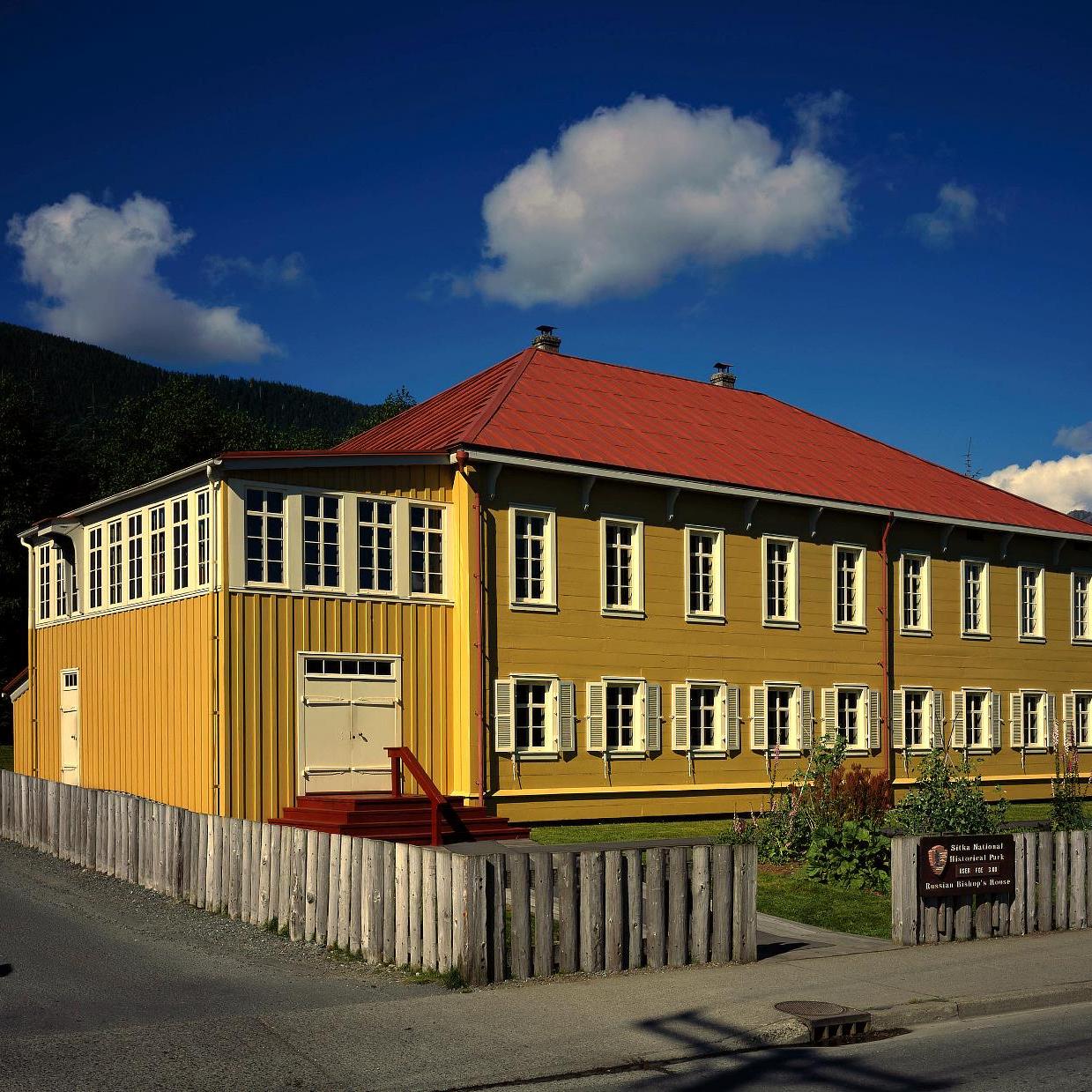 Two-story historic building with yellow walls and red metal roof.