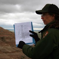 a ranger points at a geologic column on a piece of paper in front of a badlands butte.