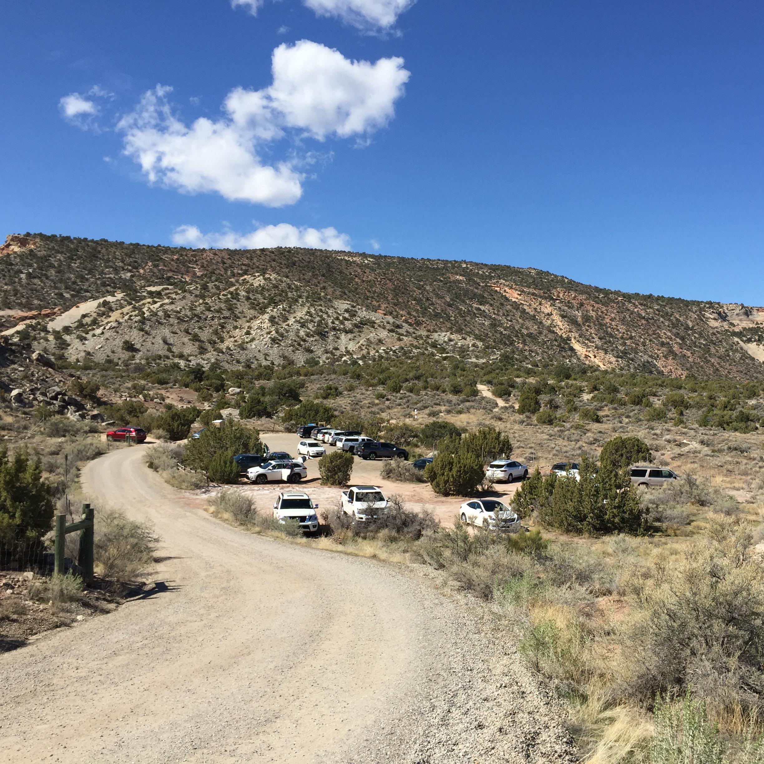 gravel road leads to dirt parking lot, backdrop of sparsely vegetated canyon slops